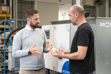 Zwei Männer sprechen miteinander über ein Brikett vor einer GROSS Brikettpresse