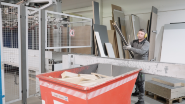 Ein Tischler wirft Spanplatten Reste in eine rote Kiste